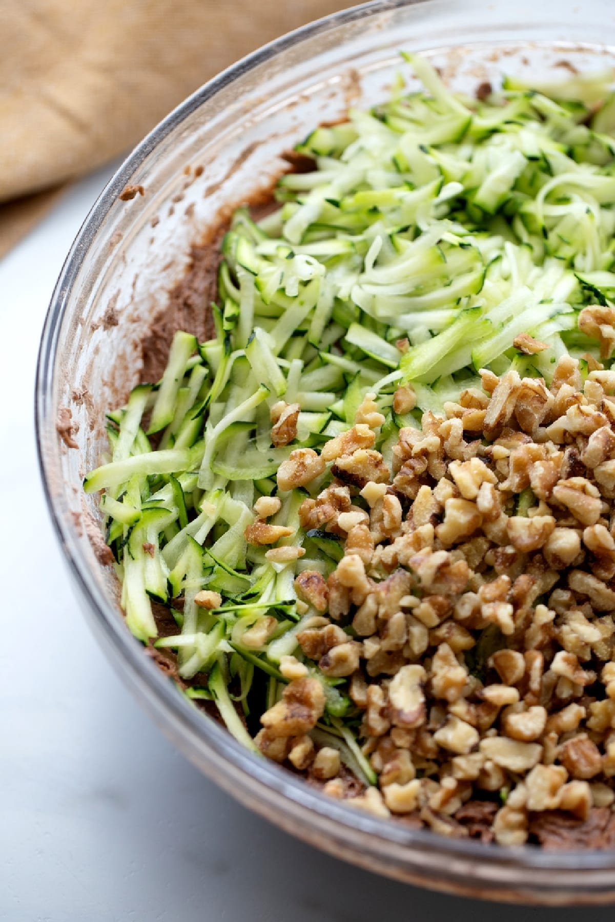 Freshly shredded zucchini and chopped walnuts being folded into chocolate cake batter.