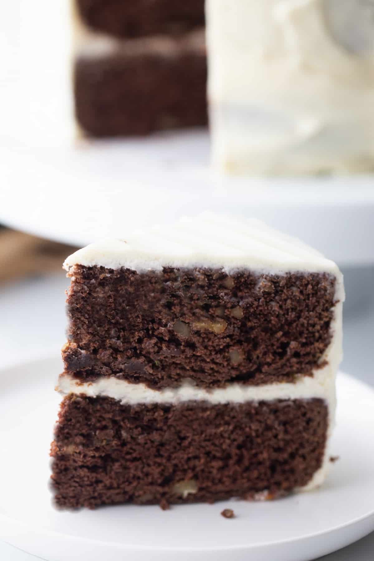 Straight-on view of chocolate zucchini cake slice showing moist texture, frosting layers, and bits of walnut.