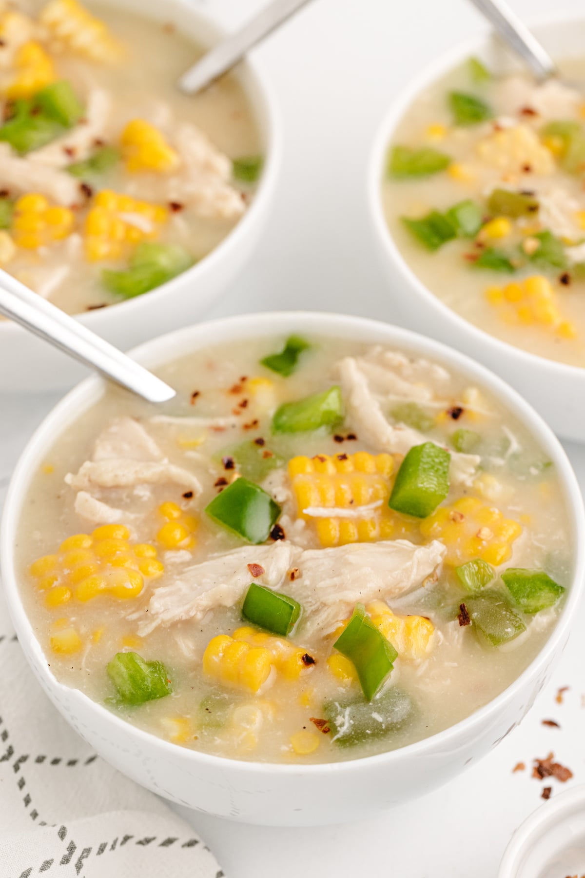 Close-up of chicken corn chowder with shredded chicken, fresh sweet corn, green bell peppers, and crushed red pepper flakes.