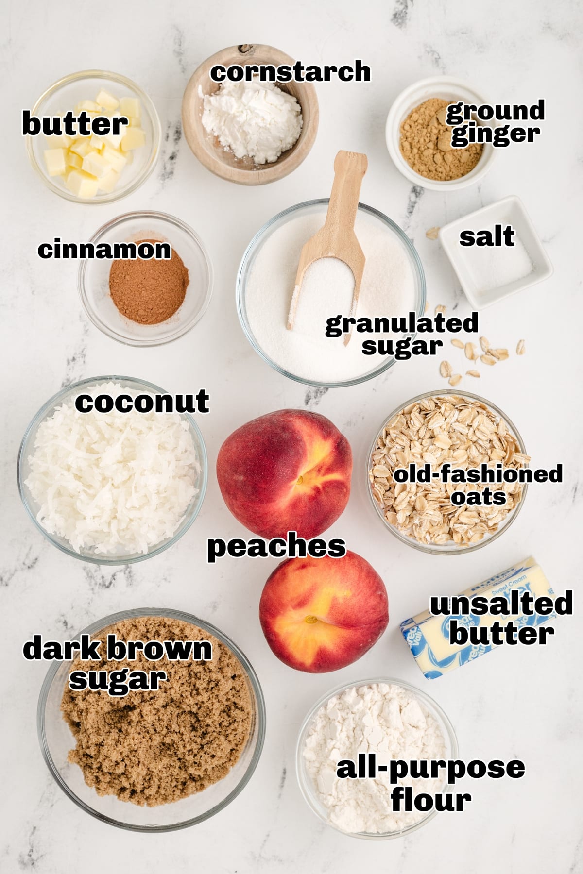 Overhead view of labeled ingredients for coconut peach crisp, including fresh peaches, oats, and shredded coconut.