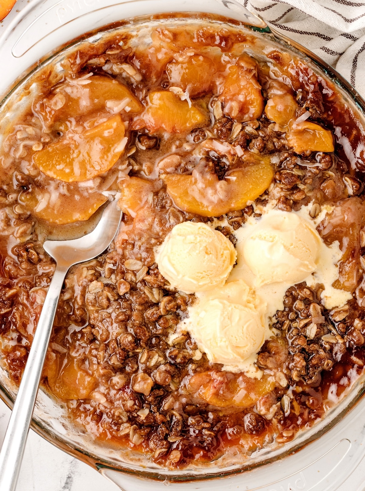 Freshly baked peach crisp in a pie dish with scoops of ice cream melting on top.