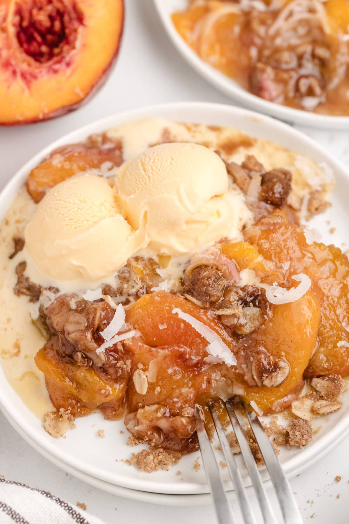 Close-up of a serving of coconut peach crisp with melting ice cream on a white plate.