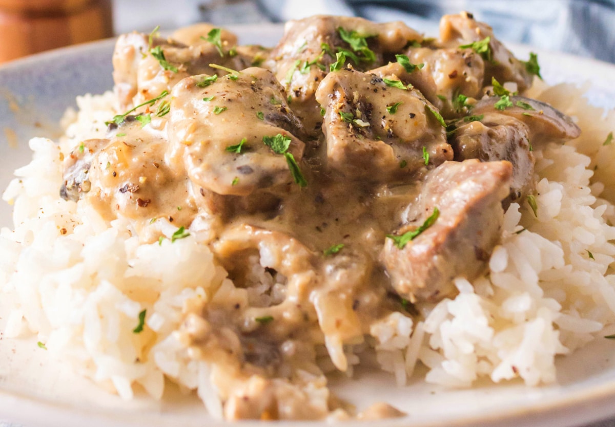 Creamy stroganoff over rice with parsley on top Overhead view of beef stroganoff on a white plate with rice and parsley garnish