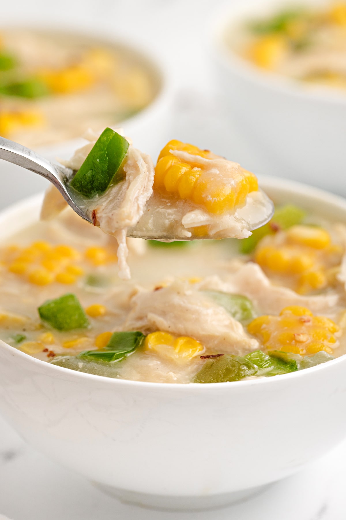 Spoonful of chicken corn chowder with shredded chicken, fresh sweet corn, green bell pepper, and creamy broth.