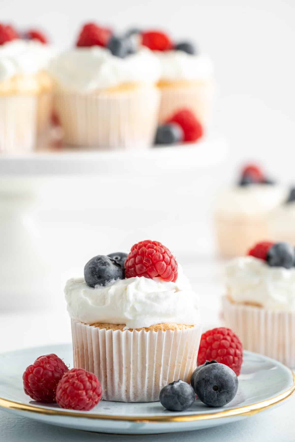 Angel food cupcake topped with homemade whipped cream, raspberries, and blueberries on a dessert plate