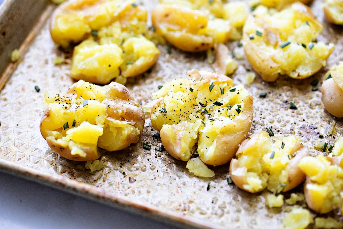 Salt and vinegar smashed potatoes on a sheet pan, crisped and seasoned with rosemary and pepper, showing their hand-smashed texture, by Noble Pig.