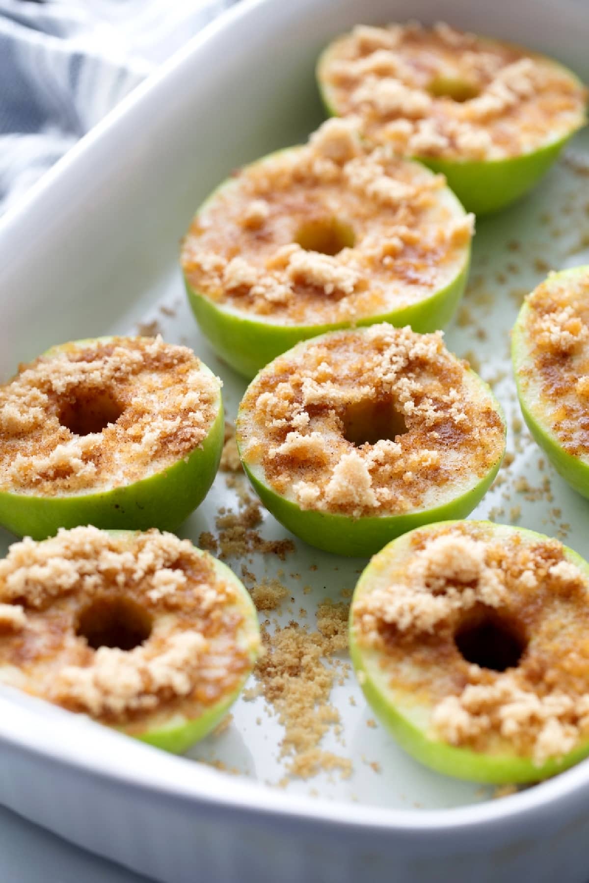 Cored Granny Smith apple halves sprinkled with brown sugar and cinnamon in a baking dish. Granny Smith apple halves topped with brown sugar and cinnamon before baking