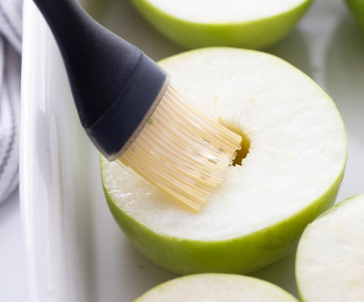 Freshly cored Granny Smith apple halves brushed with lemon juice before adding cinnamon, brown sugar and maple syrup. Brushing Granny Smith apple halves with lemon juice before baking