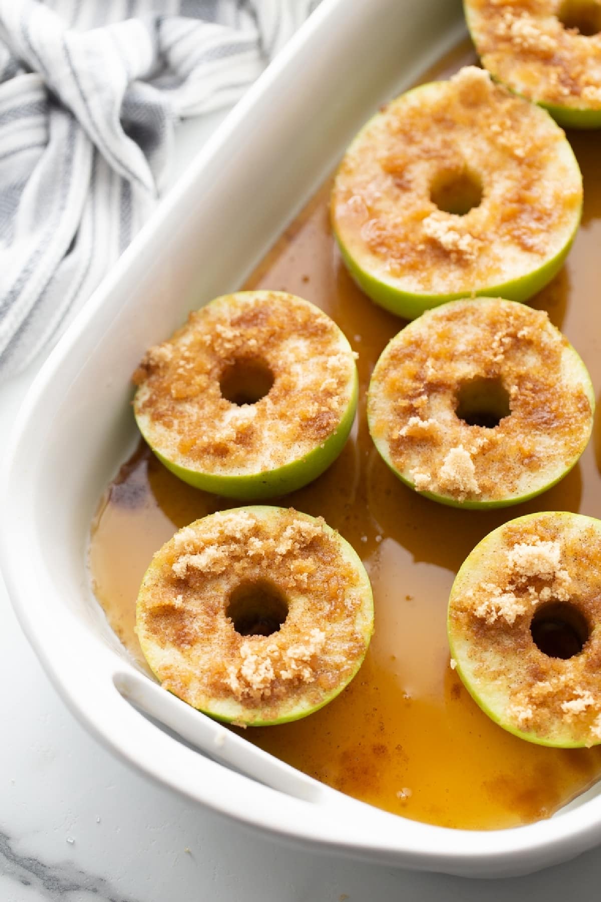 Granny Smith apple halves with brown sugar and cinnamon sitting in pure maple syrup before baking. Baked apples with maple syrup and cinnamon prepared in a baking dish