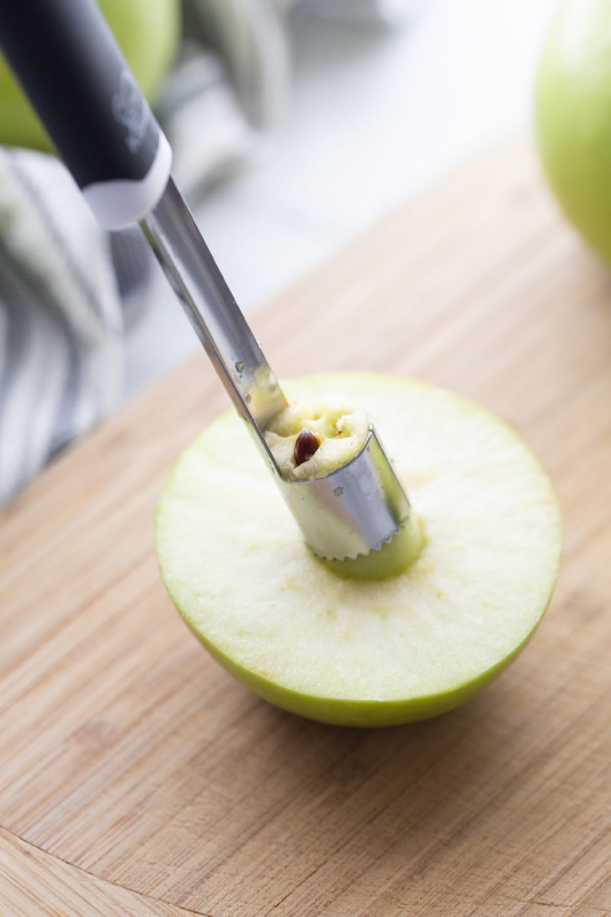 A Granny Smith apple half being cored before baking with cinnamon and maple syrup. Coring a Granny Smith apple for baked apples with maple syrup