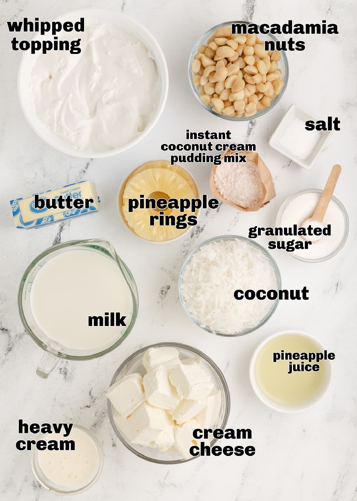 Ingredients for Hawaiian Dream Dessert Cups with macadamia nuts and coconut pudding Ingredients for Hawaiian Dream Dessert Cups including macadamia nuts, coconut cream pudding mix, pineapple rings, coconut, and cream cheese arranged on a marble surface.