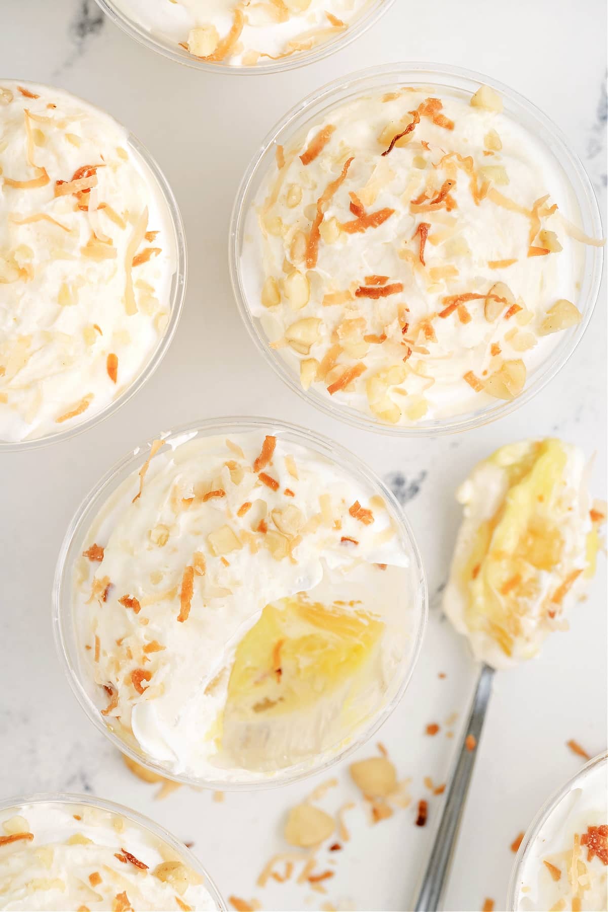 Hawaiian Dream Dessert Cups showing creamy pineapple and coconut layers Overhead view of Hawaiian Dream Dessert Cups with one cup showing a spoonful removed to reveal creamy layers of pineapple and coconut.