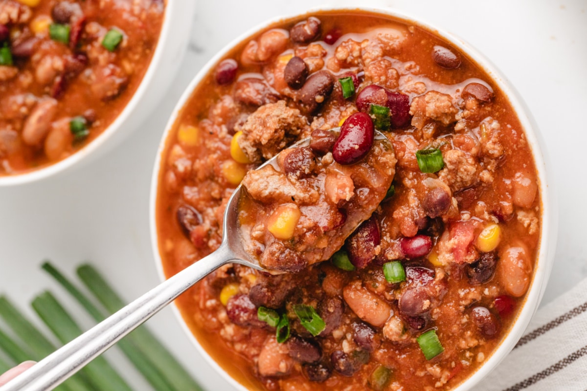 Spoonful of low calorie turkey chili with beans, corn, and green onion in a white bowl.