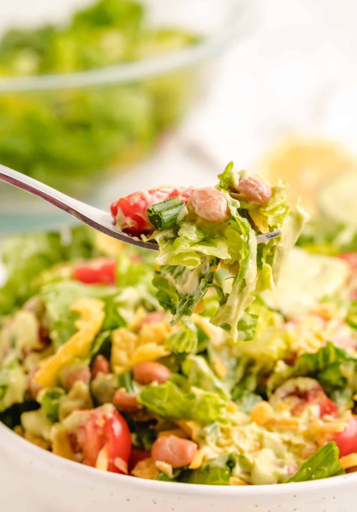 Fork over bowl of Mexican salad with avocado dressing Fork holding up lettuce from a large bowl of chopped Mexican salad with avocado dressing