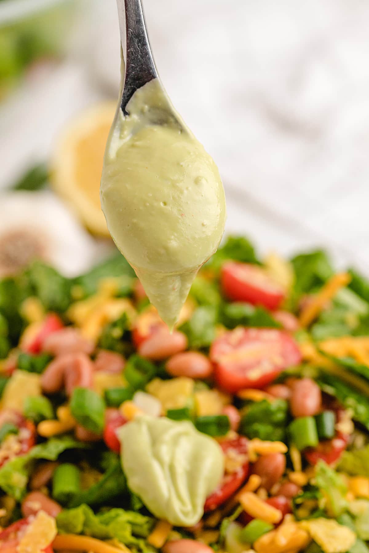 Spoon showing thick texture of creamy avocado salad dressing Thick spoonful of avocado dressing in a small bowl with a spoon dipped in the center