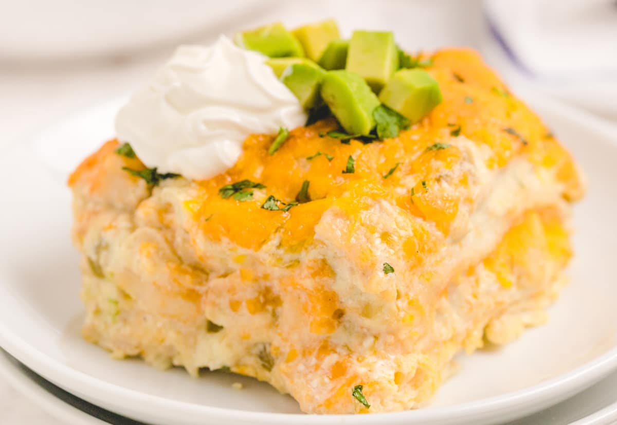 Slice of Green Chile Chicken Enchilada Casserole with garnishes Plated slice of Green Chile Chicken Enchilada Casserole topped with avocado and sour cream