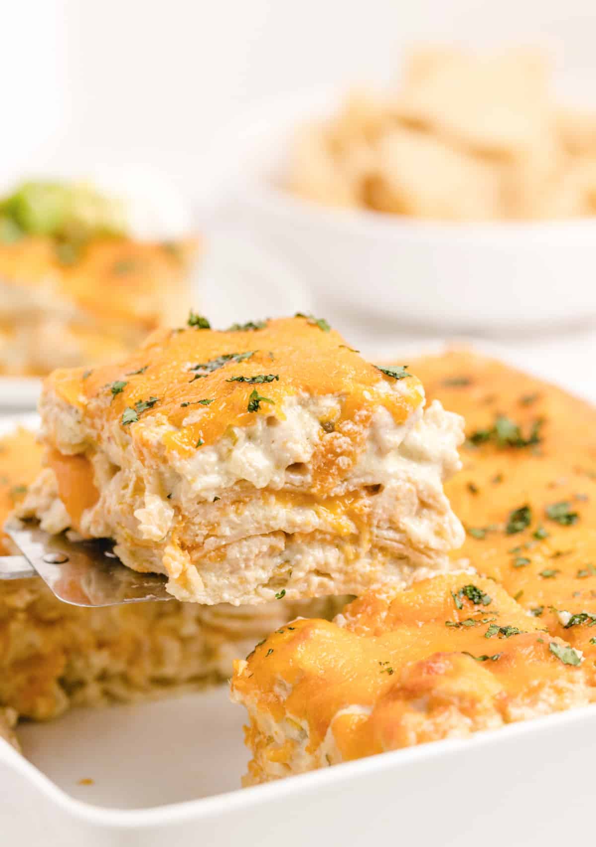 Green Chile Chicken Enchilada Casserole with a slice coming out of the pan Green Chile Chicken Enchilada Casserole with a slice being lifted out on a spatula