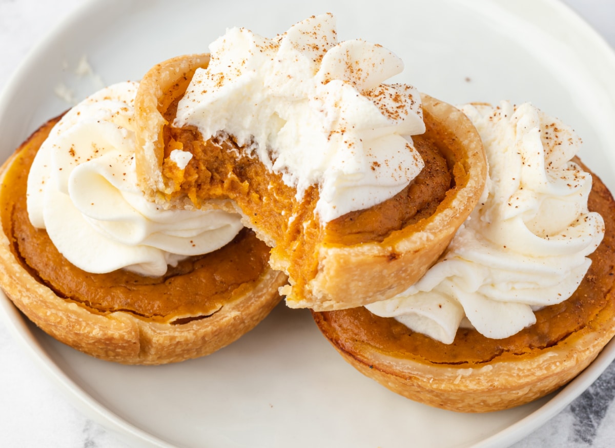 Inside of Mini Pumpkin Pie A mini pumpkin pie with a bite showing creamy pumpkin filling and flaky crust topped with whipped cream.