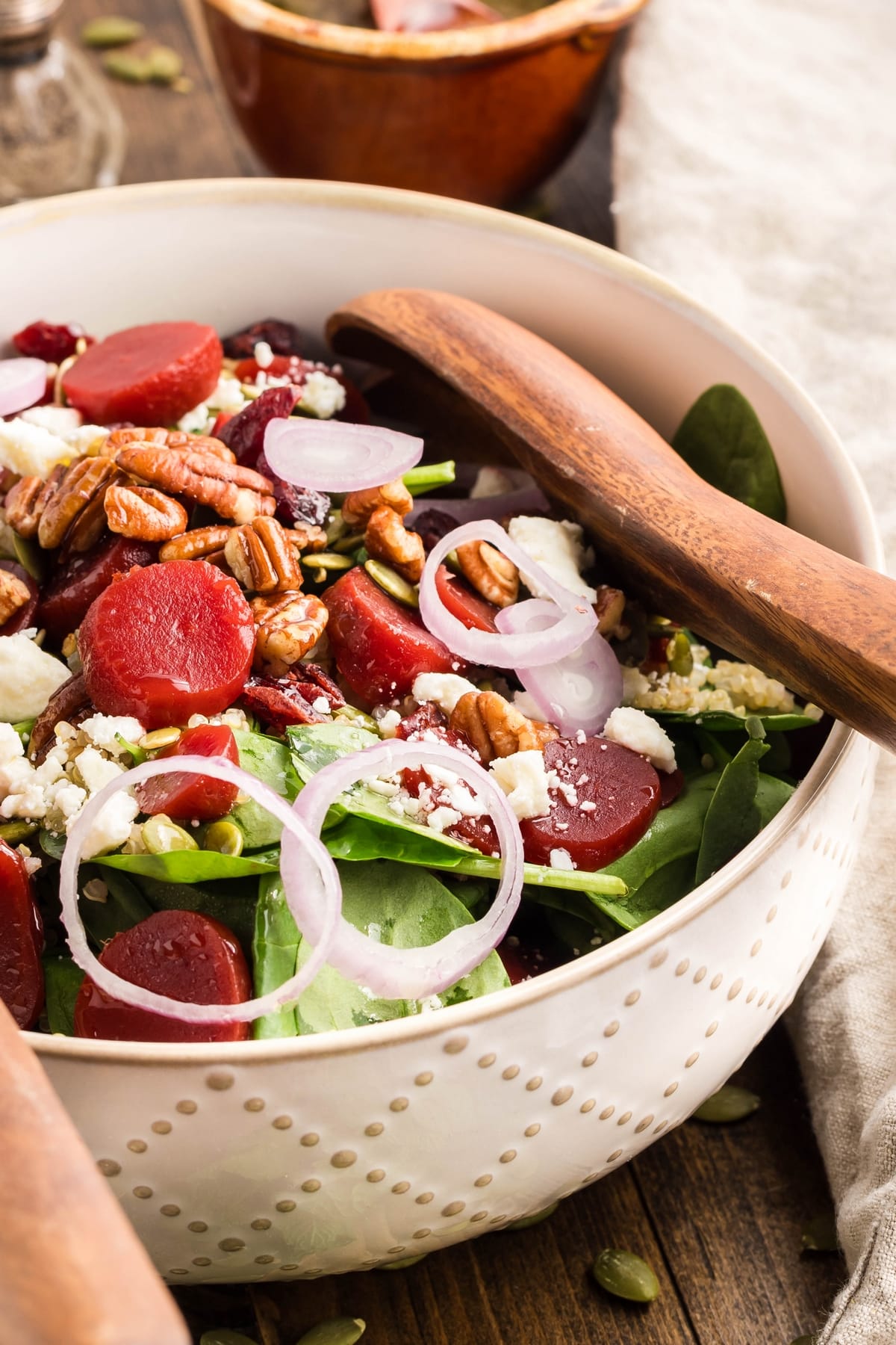 Beet salad in white bowl with salad servers Close-up view of beet salad in a white bowl, featuring vibrant beets, feta, and crunchy toppings, with salad servers.