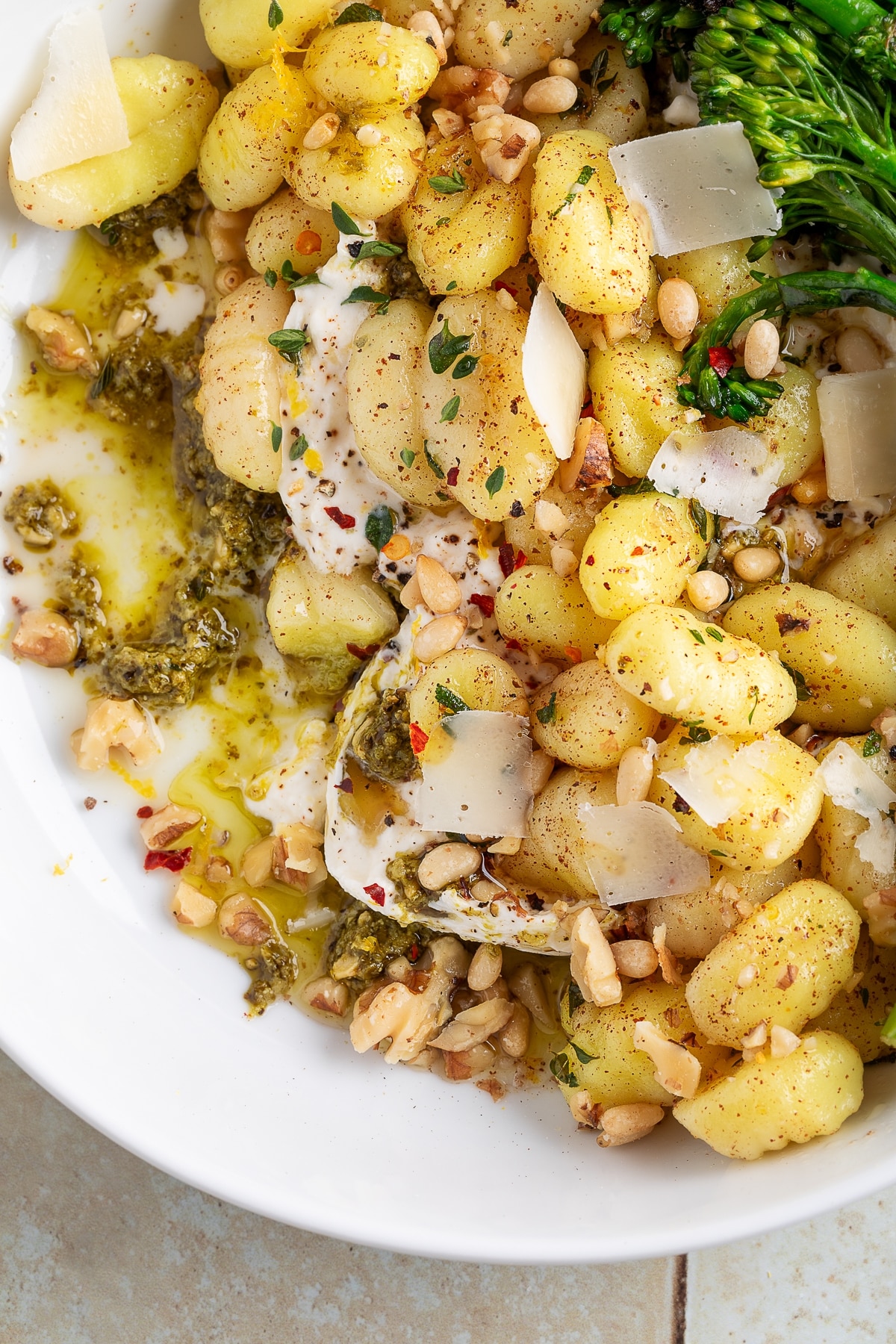 Overhead shot of gnocchi with burrata, basil pesto, toasted nuts, and parmesan shavings.