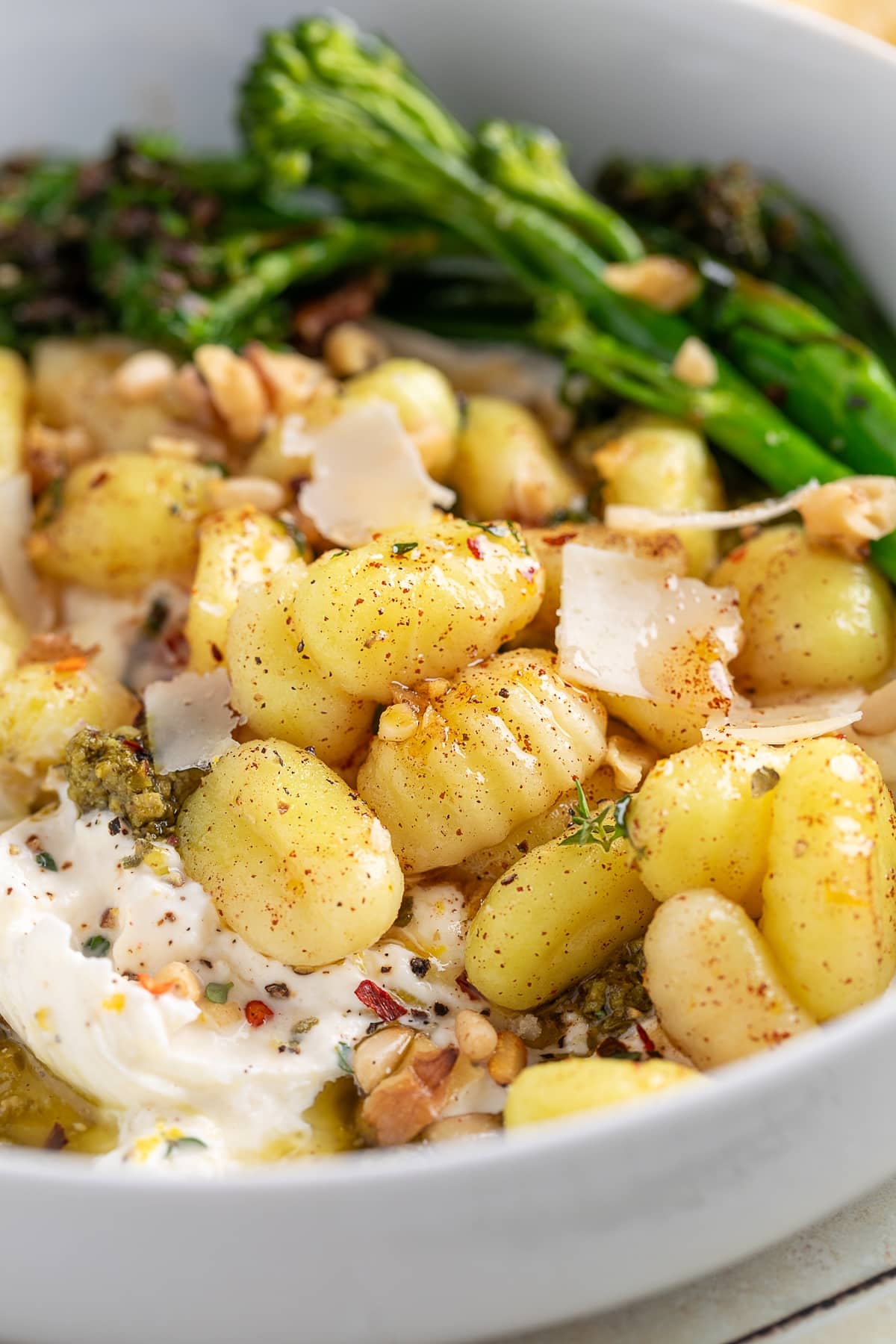 Side view of gnocchi with burrata and pesto, served with broccolini and topped with parmesan shavings.