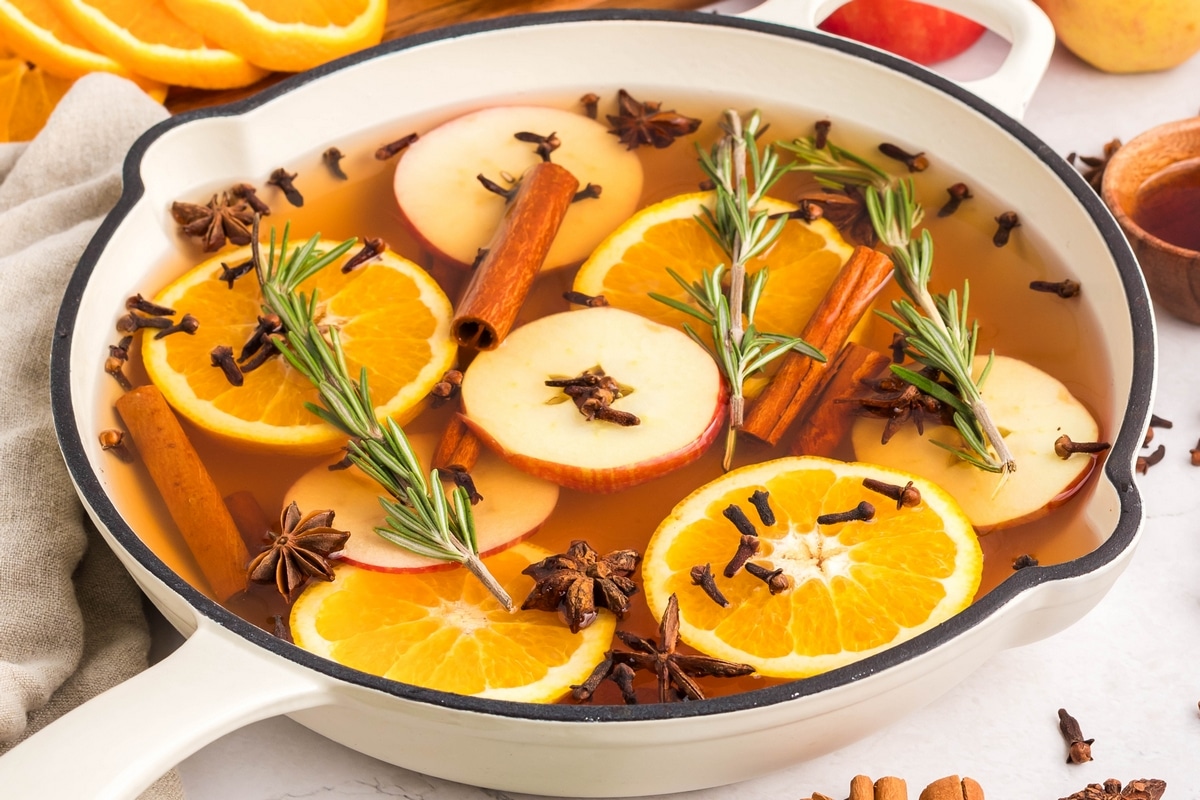  A close-up shot of a simmer pot with fresh fruit and spices in a white skillet.