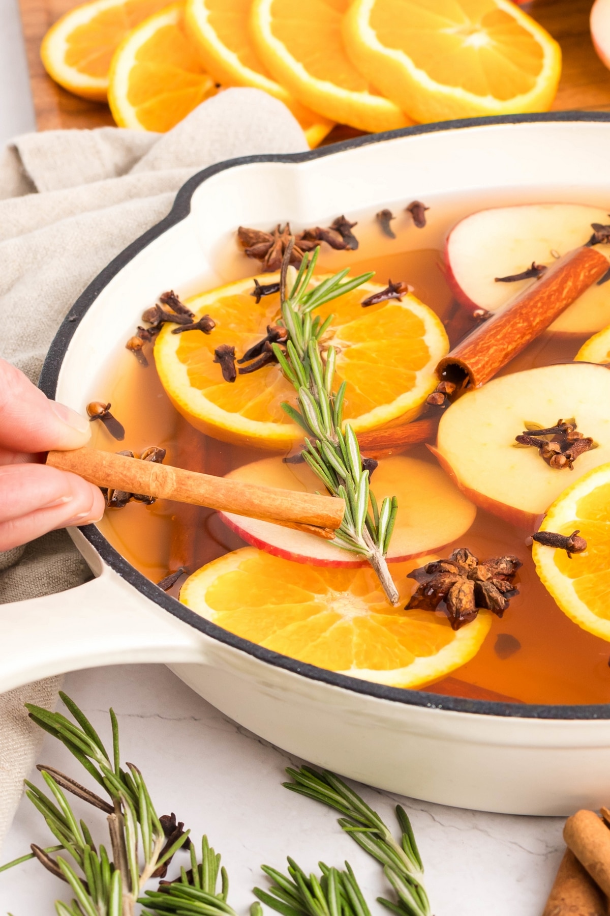 A white cast iron skillet filled with a holiday simmer pot featuring spices and citrus.