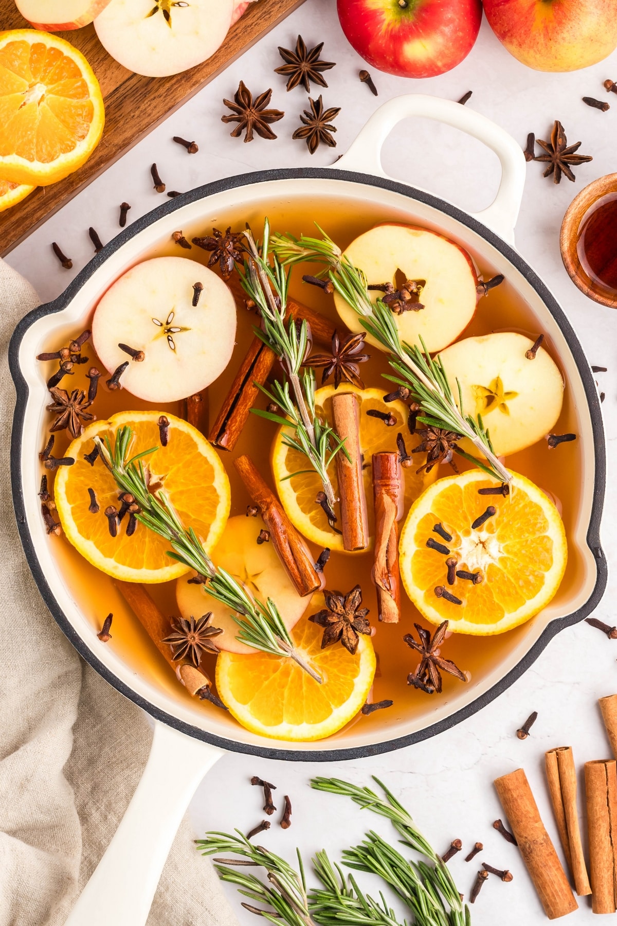 Overhead view of a holiday simmer pot in a white cast iron skillet, filled with fruits and spices.