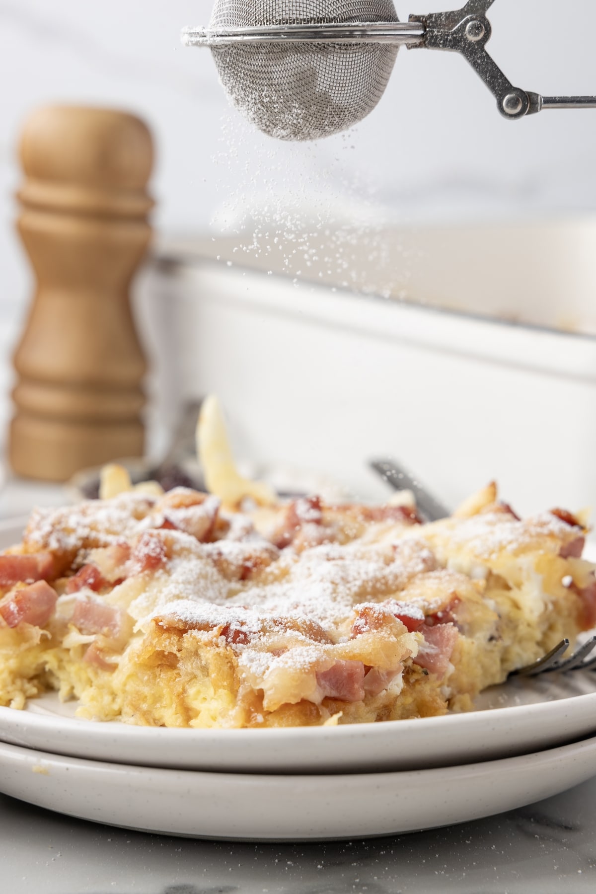 A serving of Monte Cristo Casserole being dusted with powdered sugar.