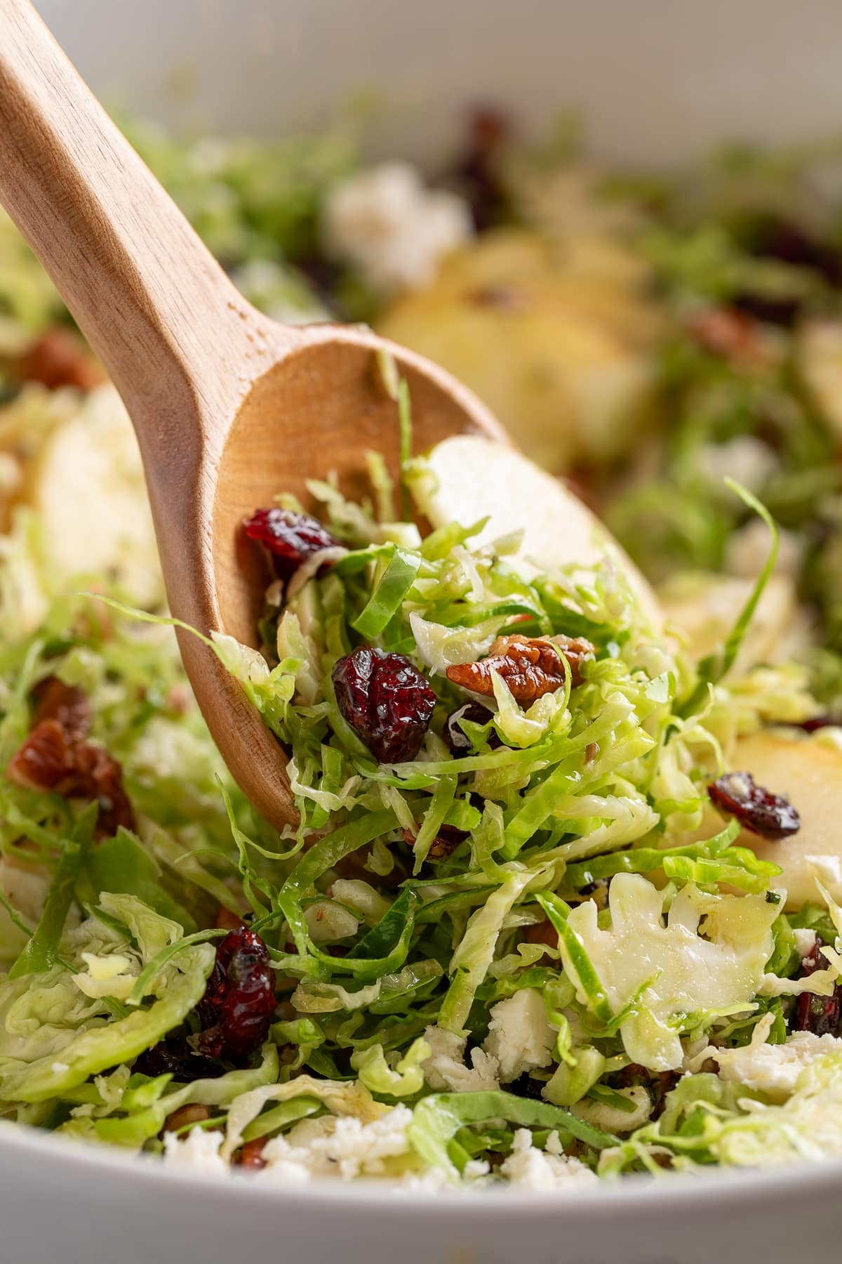 Shaved Brussels Sprouts Salad to serve wooden spoon removing some of the shaved Brussels sprouts