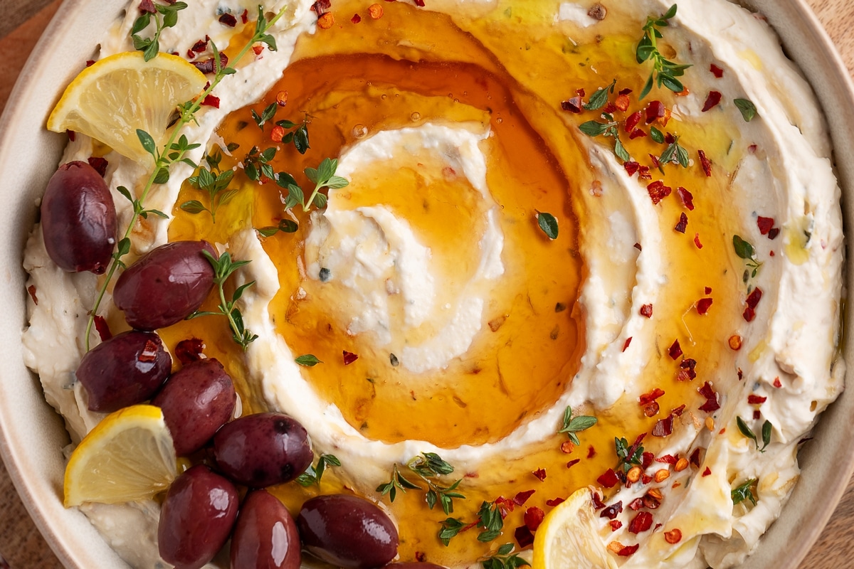 Close-up overhead shot of whipped feta roasted garlic dip with honey, topped with fresh thyme and red pepper flakes.