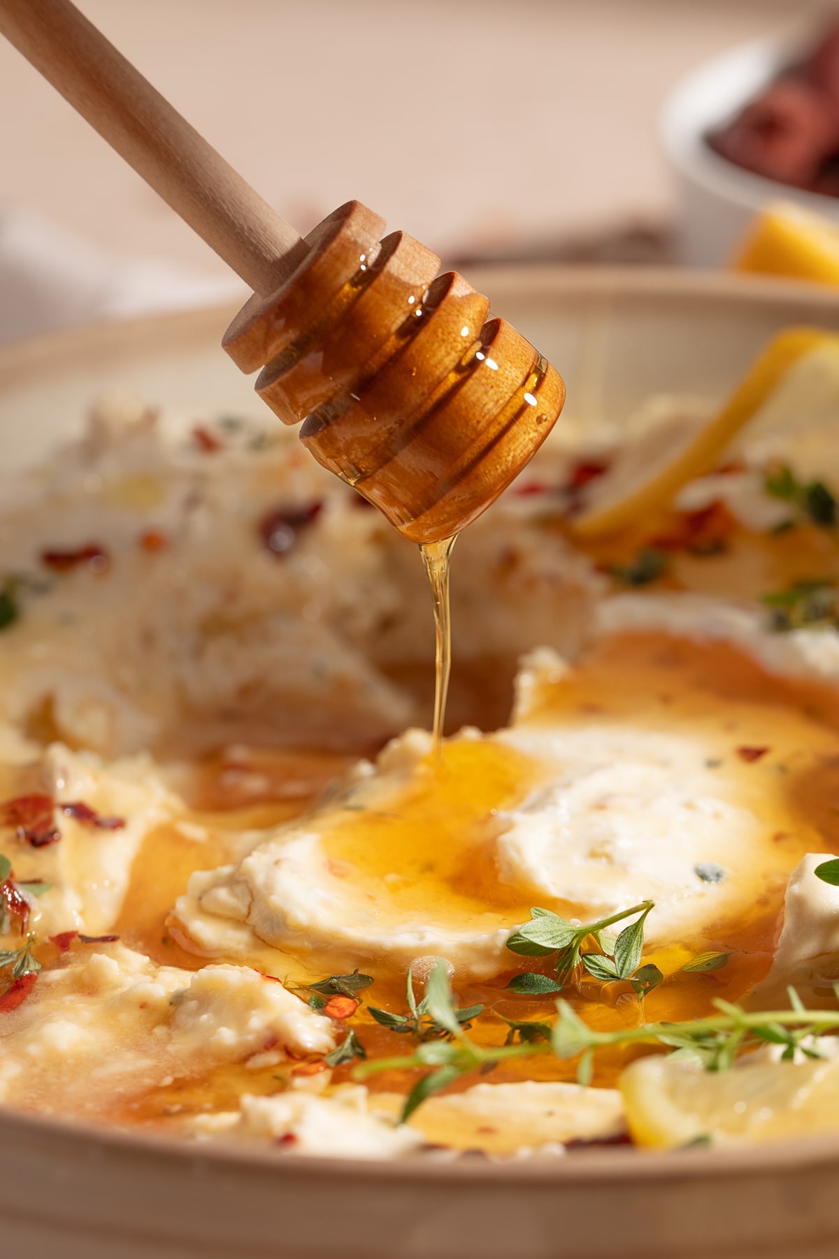 Side view of whipped feta roasted garlic dip with honey, showing a honey wand dropping honey into the dip.