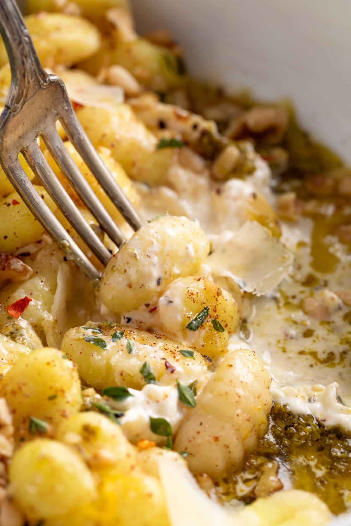 Fork twirling gnocchi over melted burrata with pesto and fresh herbs.