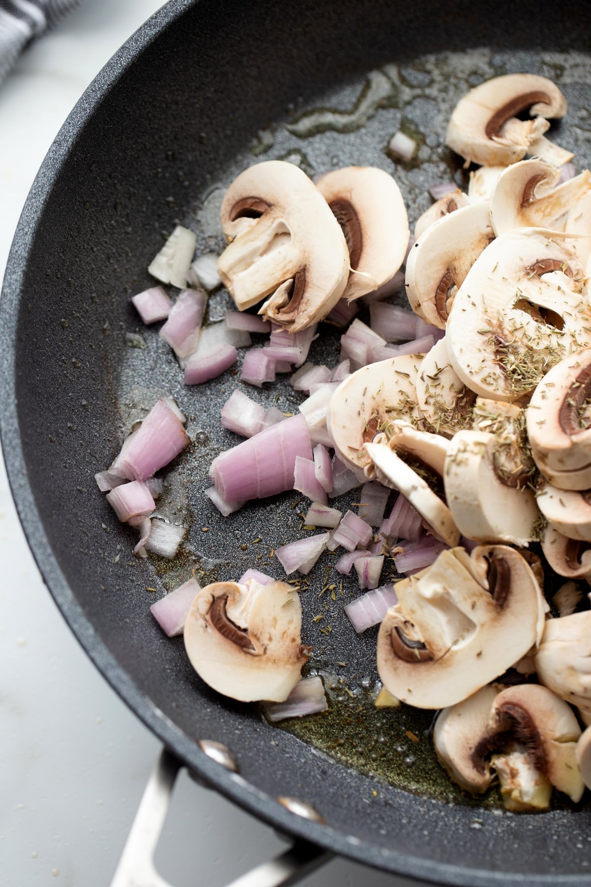 Mushrooms, shallots, and thyme cooking in a skillet for pork Marsala.