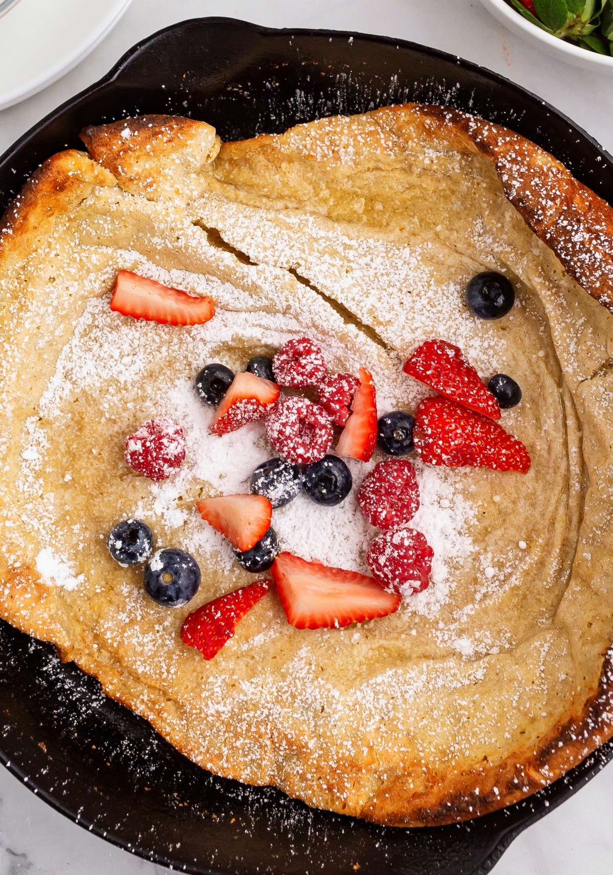 Overhead view of cast iron Dutch baby pancake topped with berries and powdered sugar