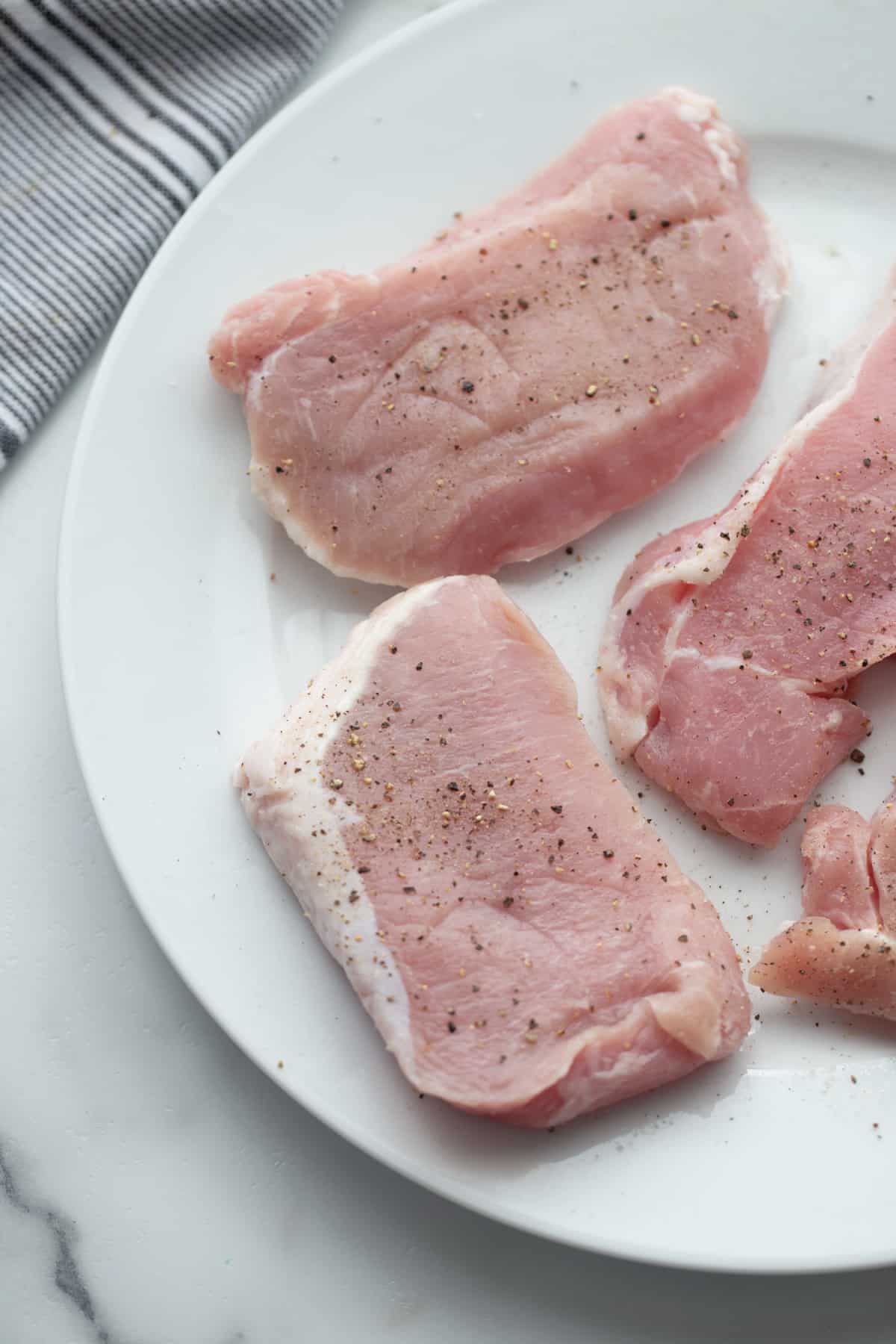 Thin boneless pork loin chops seasoned with salt and black pepper before cooking for pork Marsala.