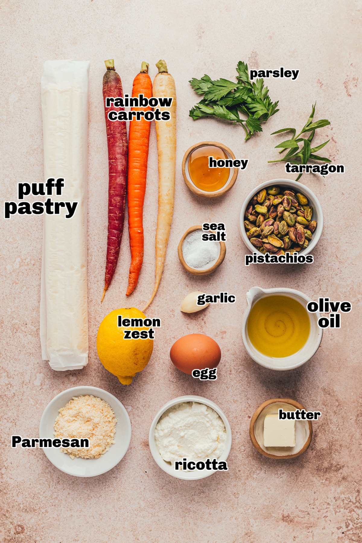 All the ingredients for the carrot tart, including puff pastry, carrots, ricotta, pistachios, herbs, and lemon, arranged on a kitchen counter.