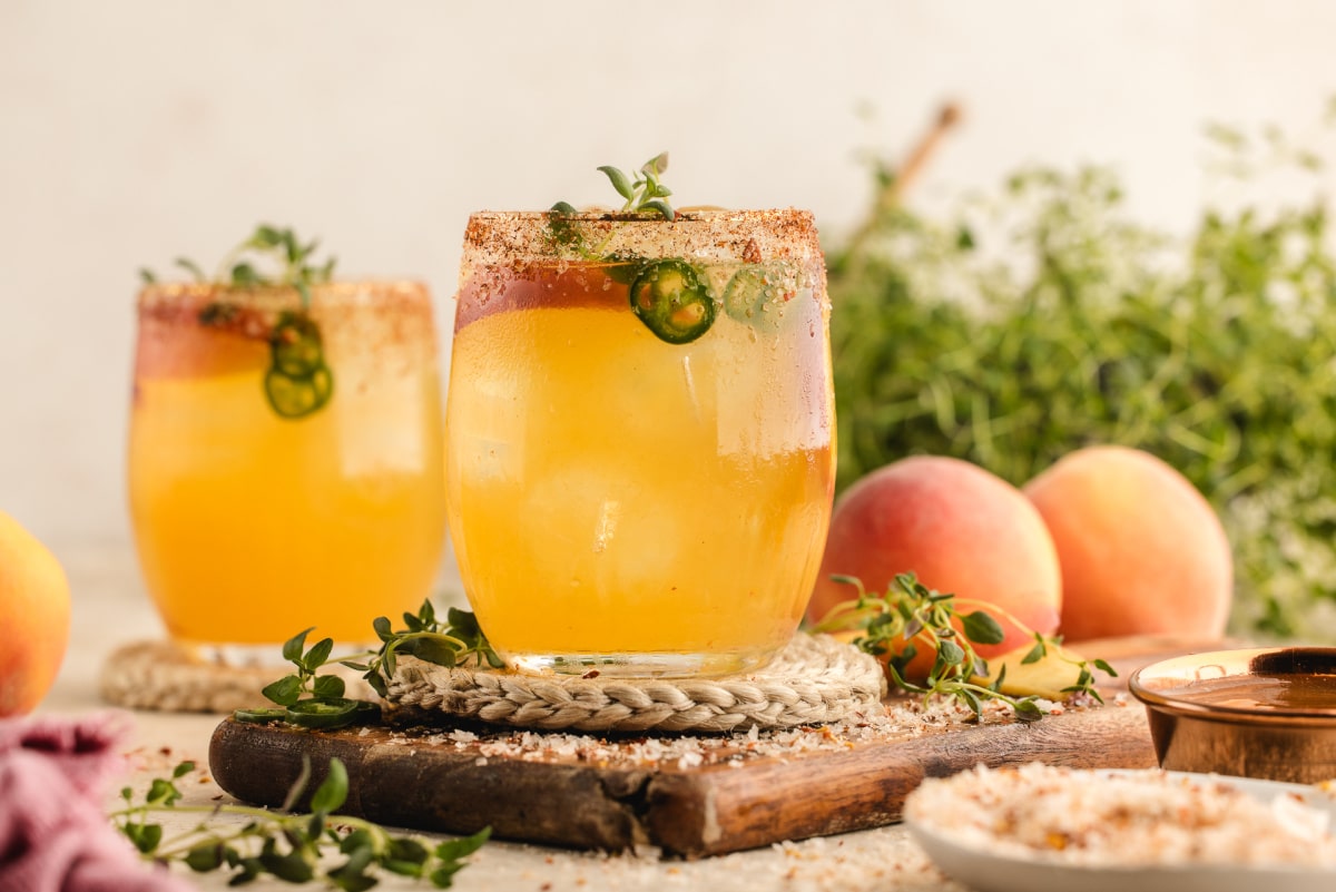 Side view of the cocktail in a short glass, highlighting the golden peach hue and fresh garnishes.
