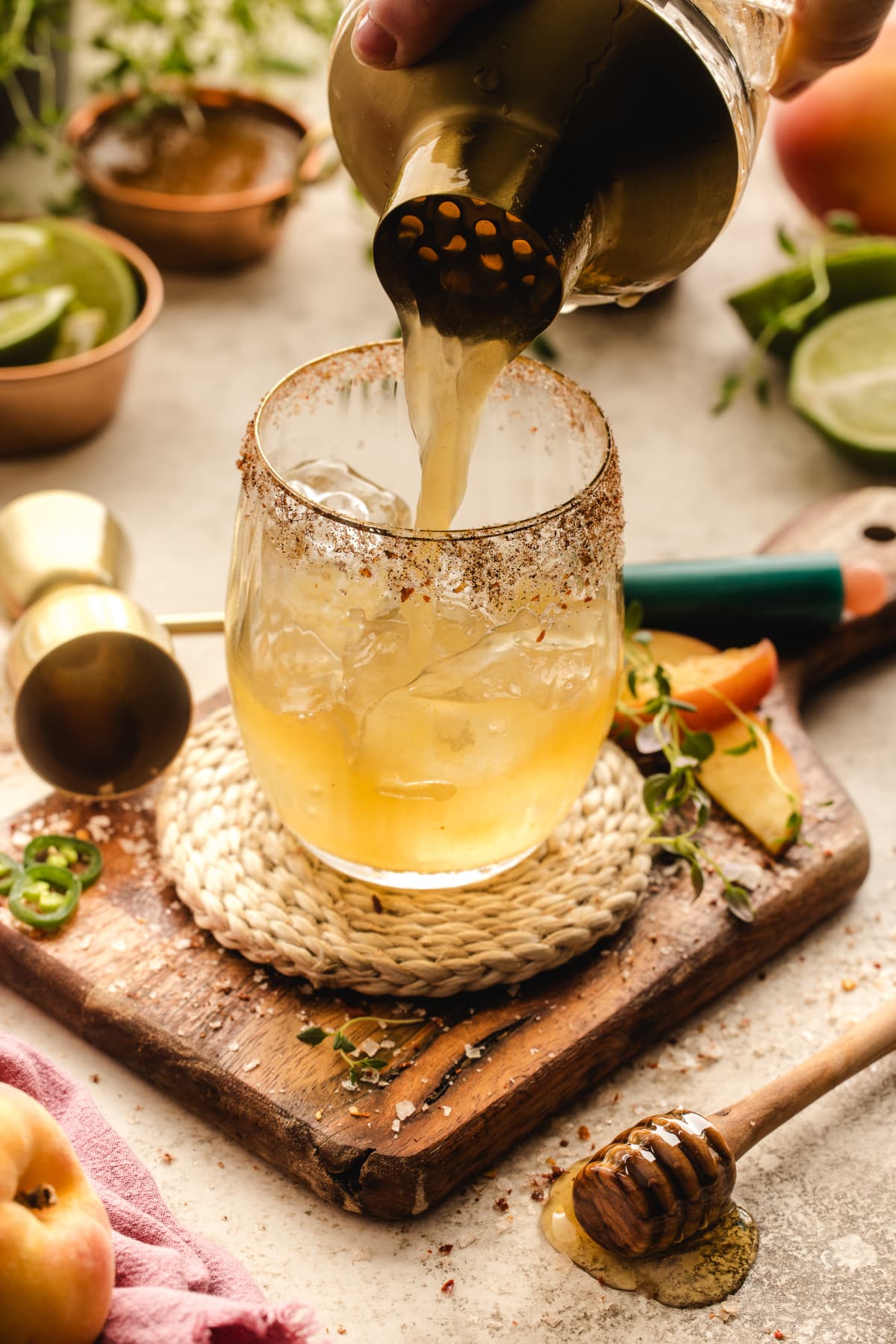 A glass being filled with the margarita as the cocktail is poured over ice, with garnishes nearby.