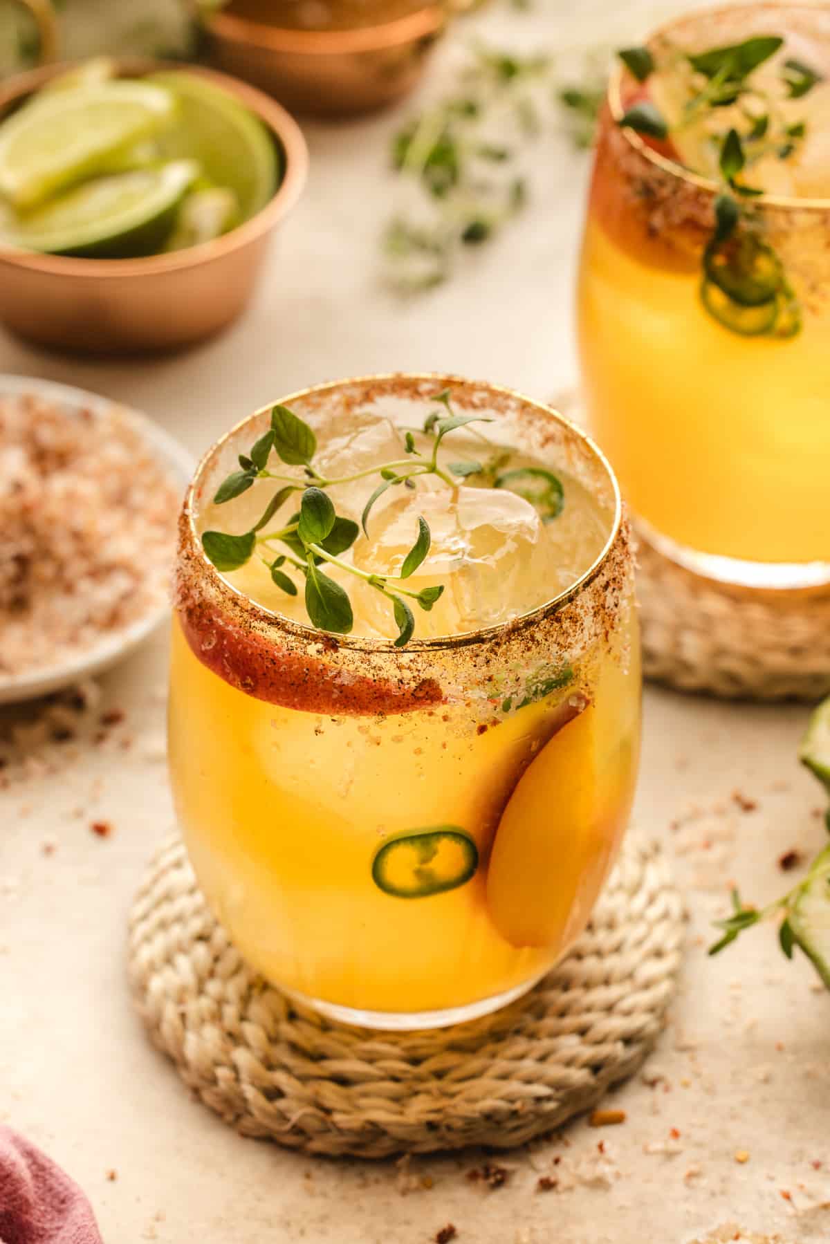 Multiple glasses of Hot Honey Peach Margaritas on a table, ready to be served, with chili salt rims and fresh peach slices.