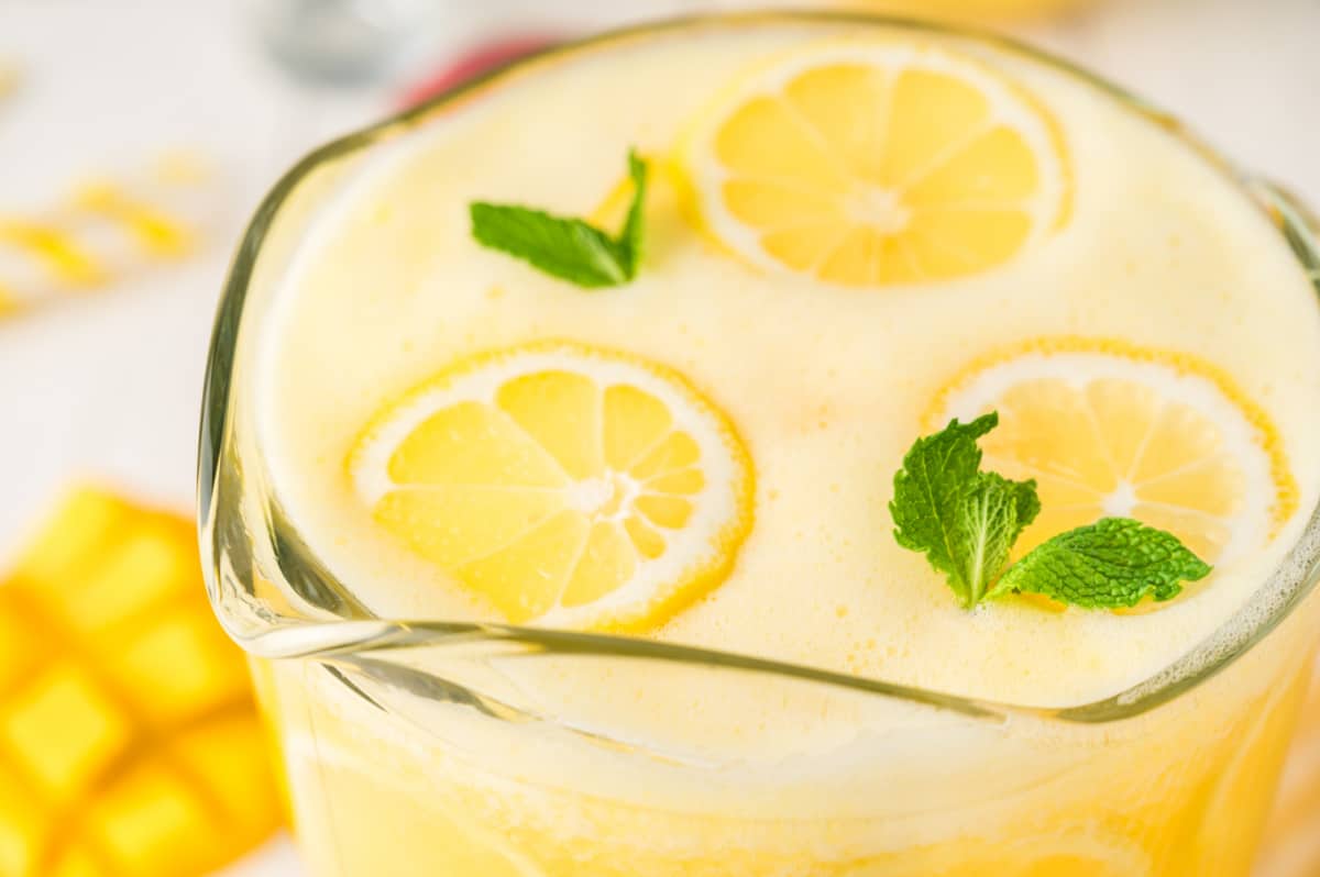 A top-down view of a pitcher of mango lemonade, showing the vibrant color and floating lemon slices.