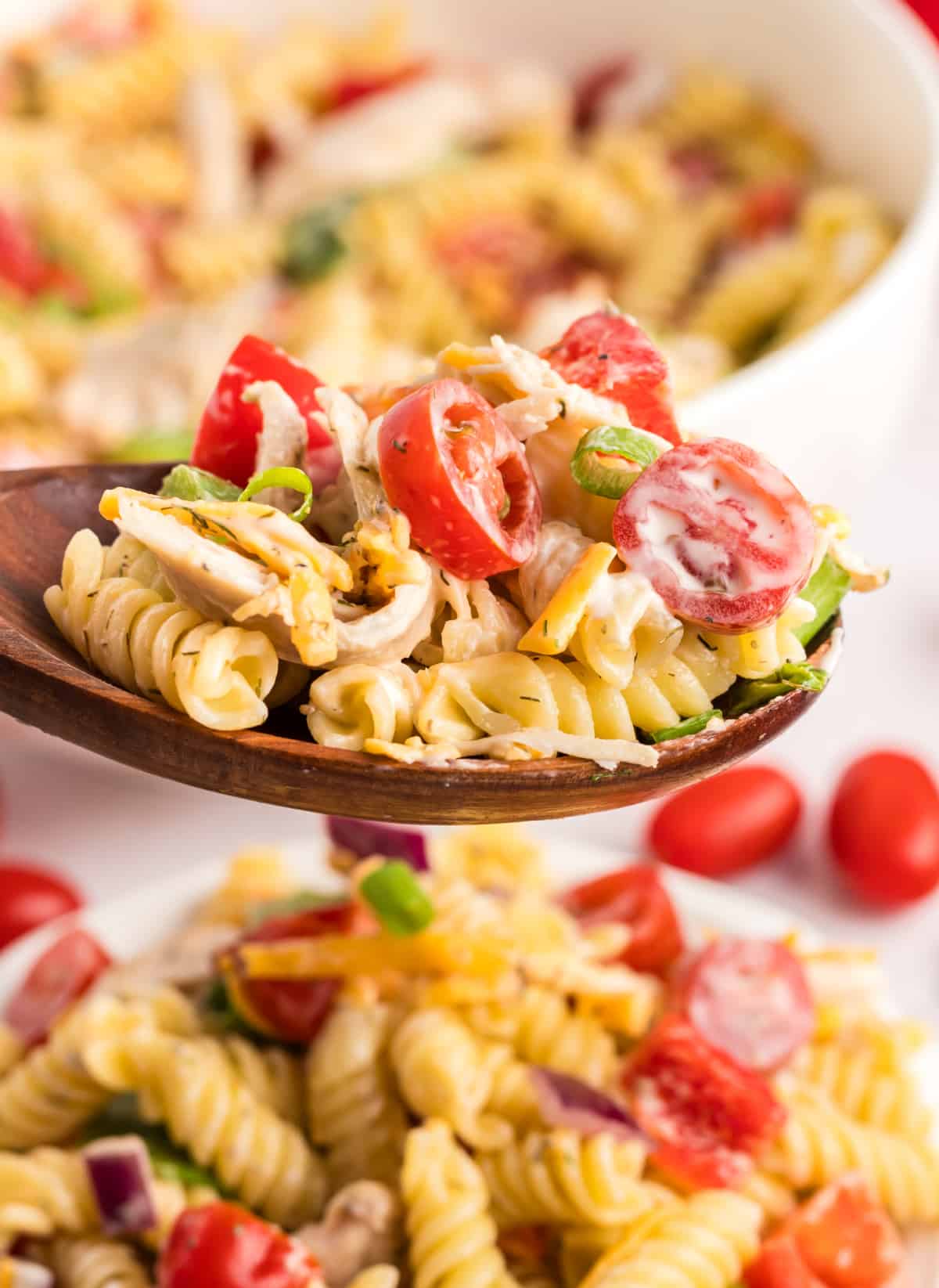 A spoonful of Chicken Ranch Pasta Salad Side angle of a wooden spoon holding a scoop of chicken ranch pasta salad with visible veggies and pasta.