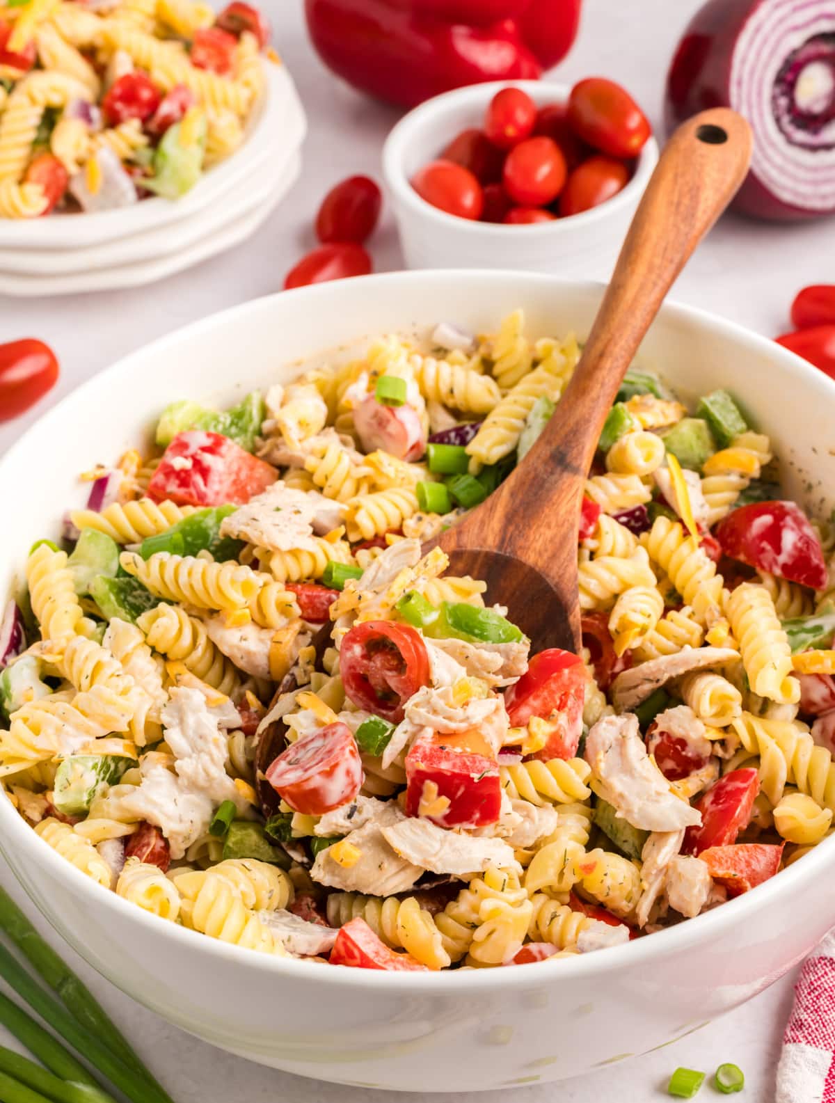 A bowl of Chicken Ranch Pasta Salad Chicken ranch pasta salad in a white bowl with a wooden spoon resting inside