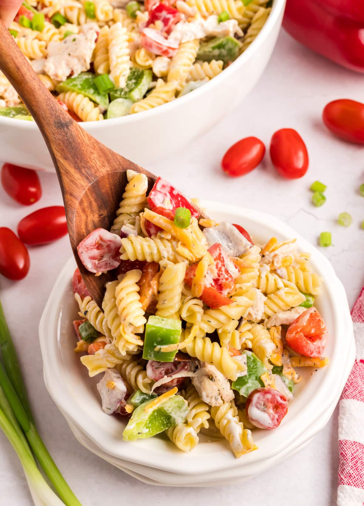 Chicken Ranch Pasta Salad on a serving plate Wooden spoon serving chicken ranch pasta salad onto a white plate.