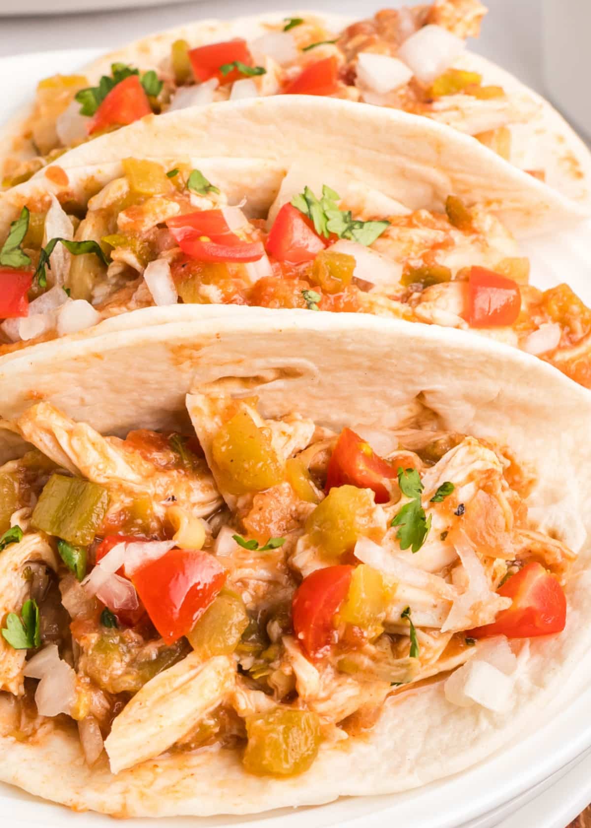 Overhead view of shredded taco chicken served in soft flour tortillas with toppings.