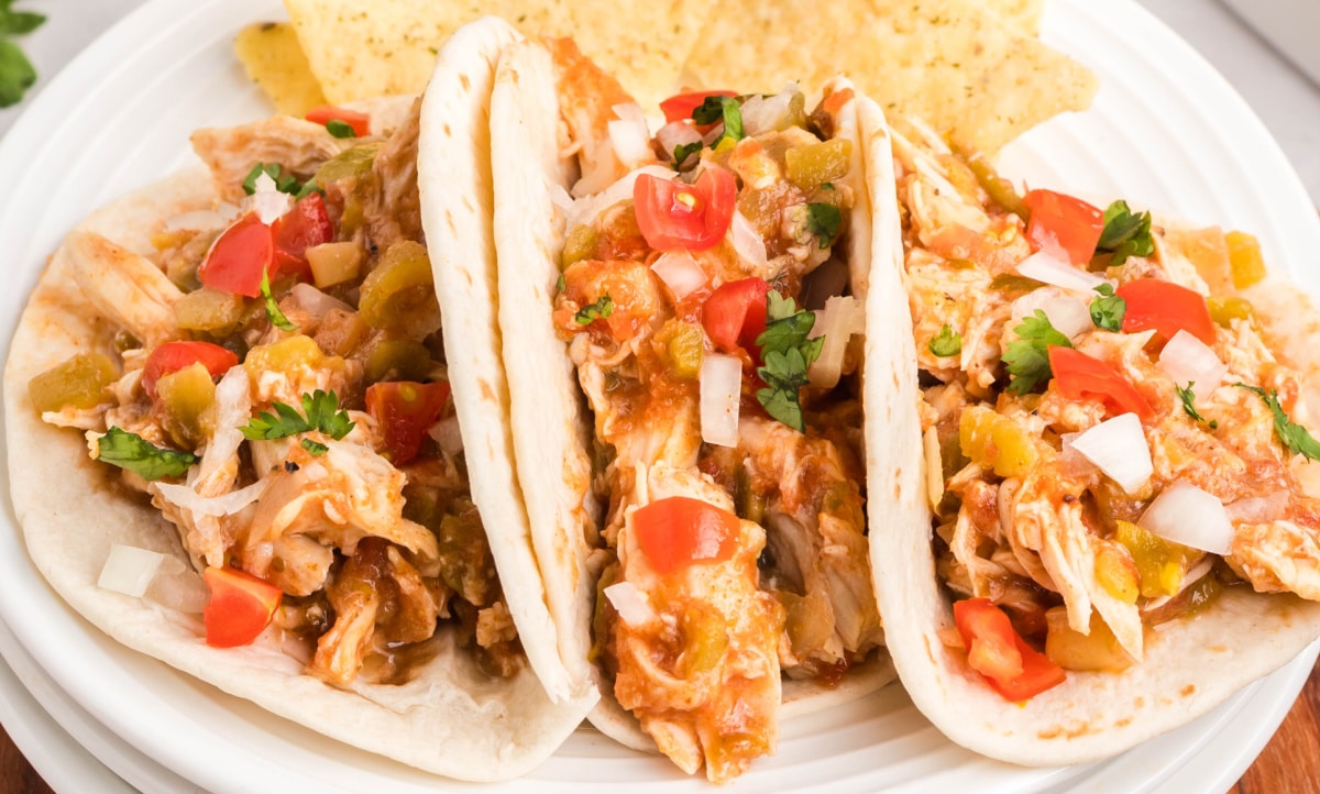  Close-up shot of slow cooker taco chicken tucked into flour tortillas with fresh garnishes.