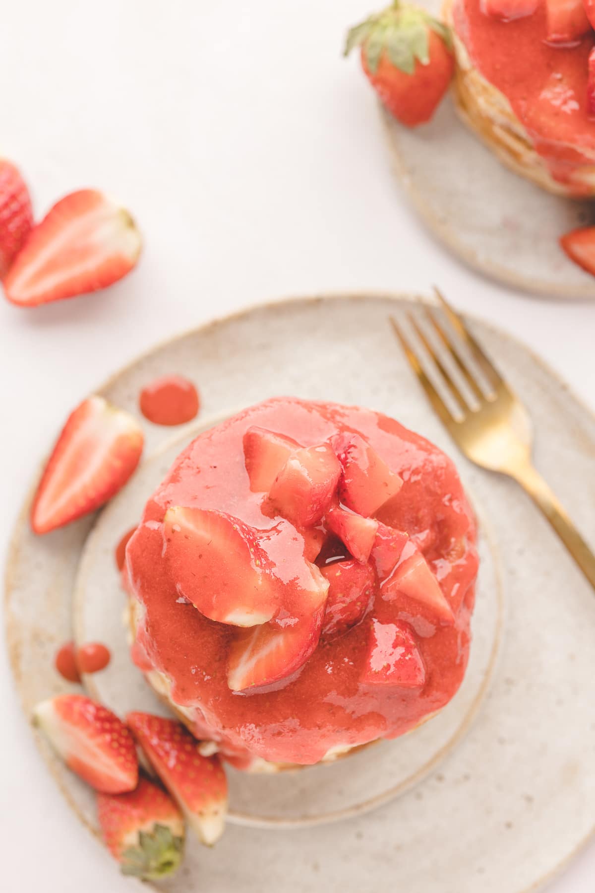 Strawberry Pancakes with Fresh Strawberries Overhead view of strawberry pancakes covered in warm strawberry sauce and topped with fresh sliced strawberries on a ceramic plate.