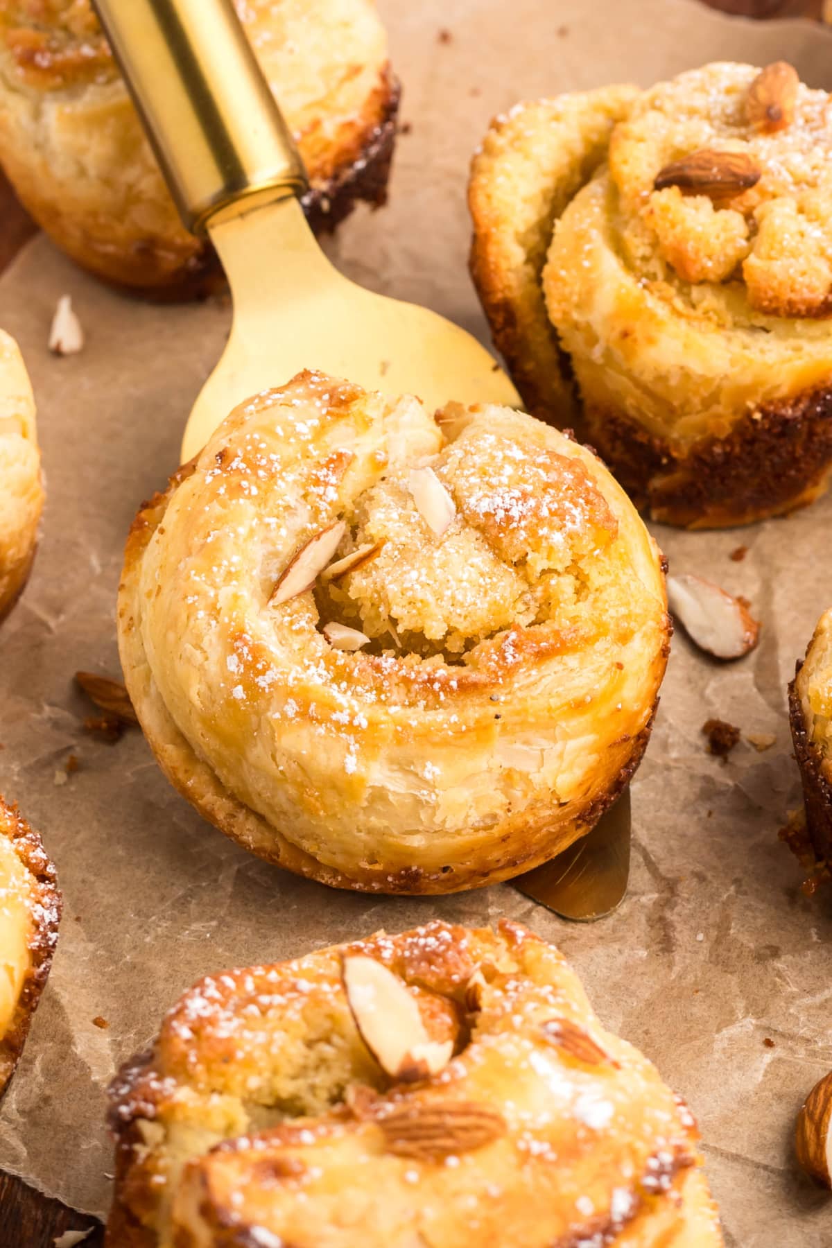 serving almond cruffins A cruffin being lifted from a muffin tin with a metal spatula, showing off its height and layers.