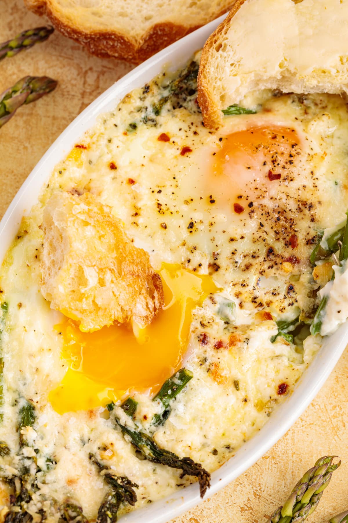 Close-up of baked eggs with a runny yolk and a piece of toast resting beside the dish, ready for dipping.