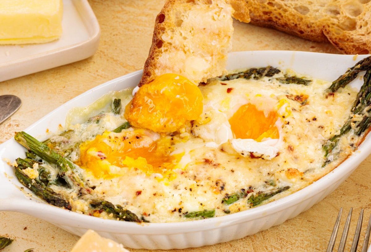 Side view of baked eggs with visible asparagus and toast positioned next to the dish. 